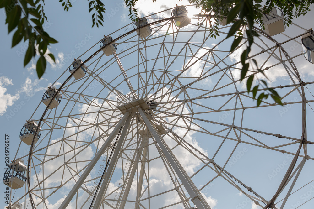 White Ferris wheel against a Sunny summer sky with white clouds.