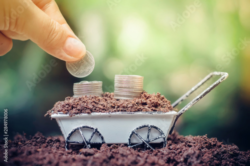  Close up of hand putting coins in stack of coins is growing up on wheel barrow for business investment or saving concept photo