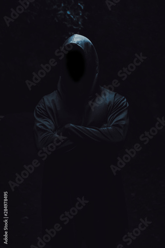 Slika na platnu A beefy man in a black robe and hood stands with his arms folded on his chest on a black isolated background