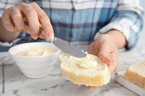 Woman spreading butter onto slice of bread over marble table, closeup
