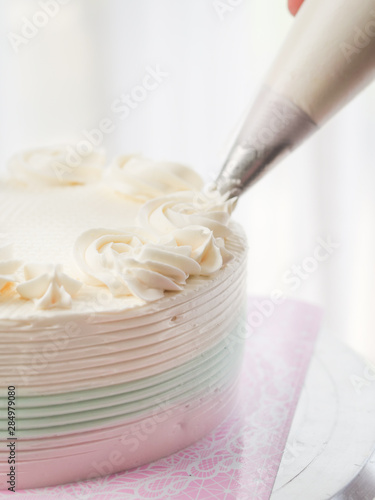 Confectioner topping cakes with cream using a pastry bag,
