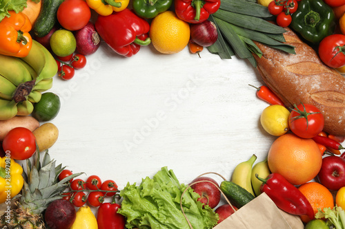 Frame of paper bag with fresh vegetables and fruits on white wooden background, top view. Space for text