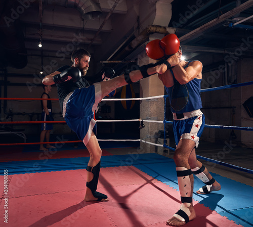 Handsome male boxer training kickboxing with sparring partner in the ring at the sport club