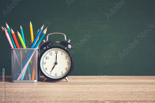 Alarm clock on wooden table on blackboard background in classroom, Back to school concept.