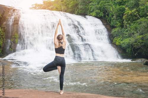 Young asain women practicing yoga at front of grand waterfall.