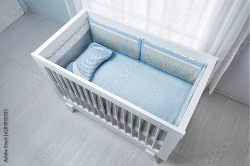 Children's bed in an empty room, lit by sunlight. There are checked mats and pillows on the bed