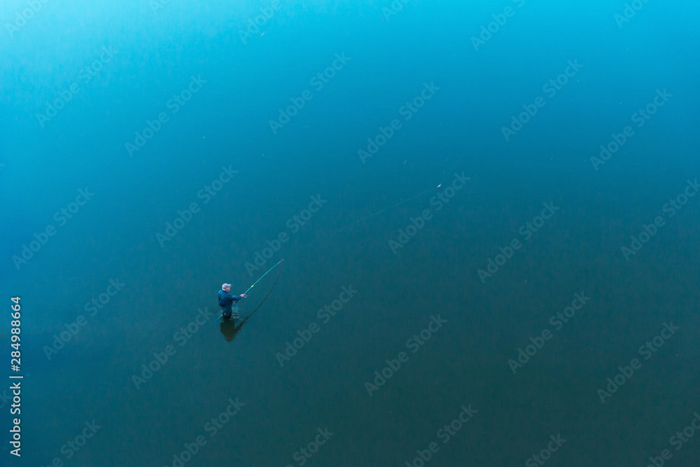 Fototapeta premium a lone fisherman standing in the water throws tackle. float rod. the view from the top. the shores cannot be seen.