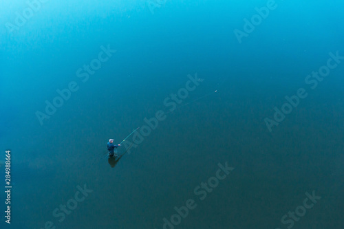 a lone fisherman standing in the water throws tackle. float rod. the view from the top. the shores cannot be seen.