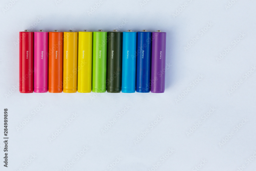 Batteries or accumulators of dimension AA or AAA of all colors of the rainbow lie or stand on a sheet of white paper. Batteries or accumulators of dimension AA or AAA of all colors of the rainbow lie or stand on a sheet of white paper.