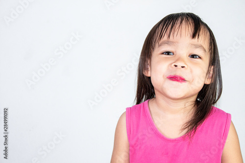Happy Asian child girl with apply red lipstick wearing pink dress isolated on white background.