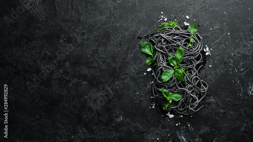 Black pasta with basil. On a black stone background. Top view. Free copy space.