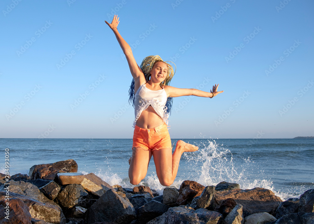 Senegalese girl with pigtails jumps on the wooden jetty on the sea. The waves are hitting the rocks and the spray is flying in different directions. Vacation. Senegalese girl with pigtails jumps on the wooden jetty on the sea. The waves are hitting the rocks and the spray is flying in different directions. Vacation.