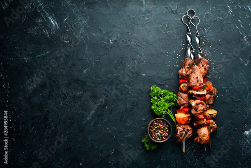 Shish kebab BBQ meat with onions and tomatoes. On a black background. Top view. Free space for your text. Rustic style. photo