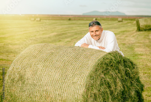 Happy man leaning on a green round hay bale in the countryside