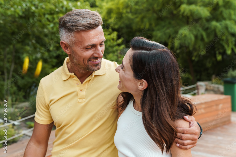 Portrait of smiling middle-aged couple looking at each other and hugging while walking in summer park Portrait of smiling middle-aged couple looking at each other and hugging while walking in summer park
