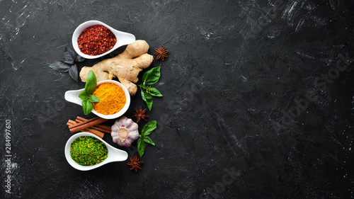 Colorful herbs and spices for cooking. Indian spices. On a black stone background. Top view.