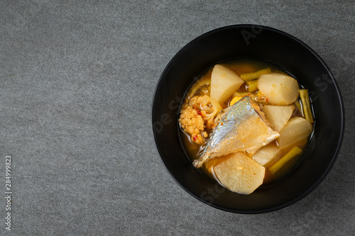 Sour curry with papaya and half fish in black bowl on the concrete table.