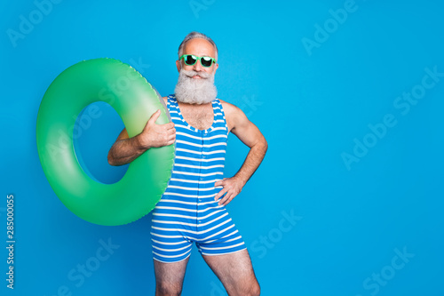 Portrait of confident man in eyeglasses eyewear holding green toy circle wearing striped swim wear isolated over blue background