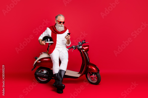 Aged macho man sit on retro moped chatting telephone wear jumper and trousers isolated red background