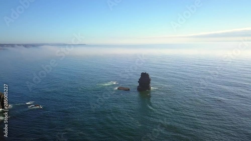 Aerial, drone shot, towards a huge rock, in middle of the Atlantic sea, fog in the background, near Arrifana Beach, on a sunny and misty morning, in Vicentina coast national park, in Portugal
