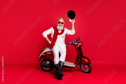 Aged macho man sit on retro moped greets every pretty lady street wear jumper and trousers isolated red background