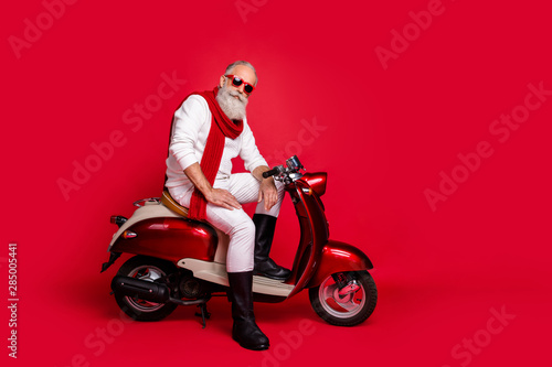 Gangster grandfather santa man sitting on retro moped wear jumper and trousers isolated red background