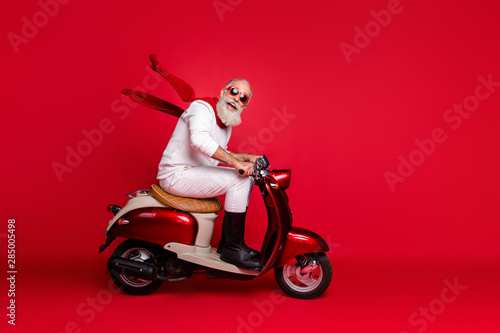 Crazy aged santa man coming newyear 2020 party by vintage moped wear jumper and trousers isolated red background
