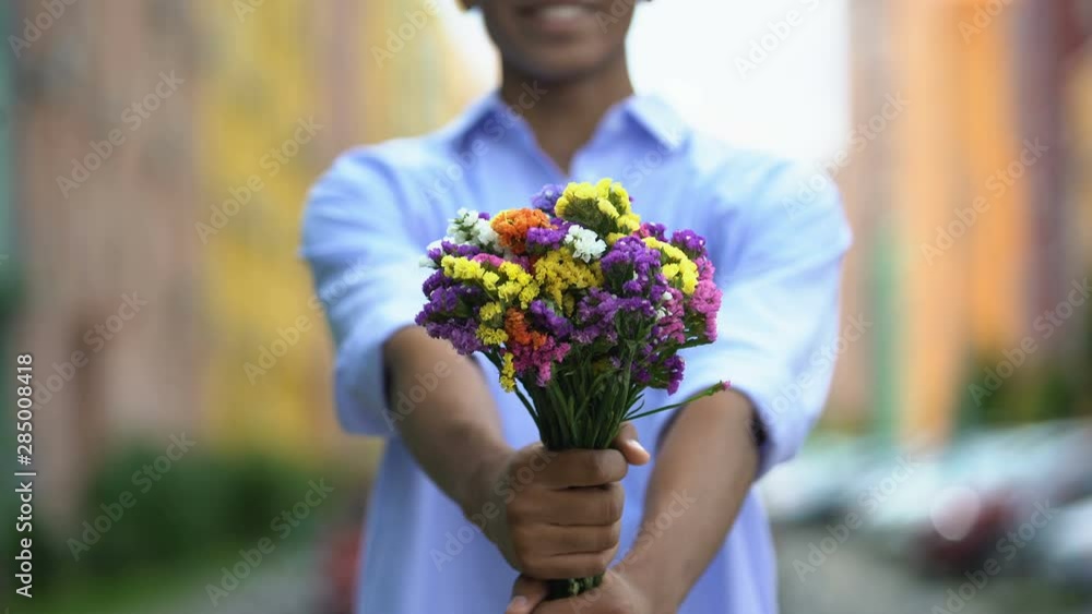 Mixed-race boy showing colored bouquet of flowers into camera, delivery, closeup Mixed-race boy showing colored bouquet of flowers into camera, delivery, closeup