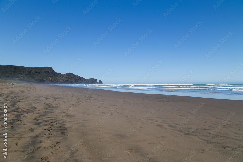 Scorching hot day at Bethells Beach, west Auckland. Black sand gets hot. Stunning summers day at Te Henga with blue sky, minimal clouds, small white caps on the waves. Looking south toward caves.