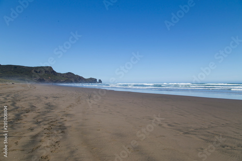 Scorching hot day at Bethells Beach  west Auckland. Black sand gets hot. Stunning summers day at Te Henga with blue sky  minimal clouds  small white caps on the waves. Looking south toward caves.