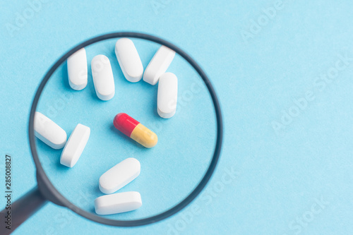 Concept - pharmaceutical testing, testing of medicines, magnifying glass, tablets on a blue background. Doping control.