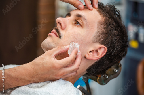 Fototapeta Naklejka Na Ścianę i Meble -  Barber closing mans pores with alum stone. Traditional ritual of after shaving the beard with alum stone. Client getting his face rubbed with alum stone after shaving in barber shop
