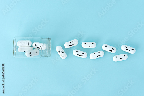 Pills with funny faces and a glass bottle on a blue background. Pharmacy antibiotic. Treating with antidepressant. Mental disorder. The concept of antidepressants and healing. Copy space.