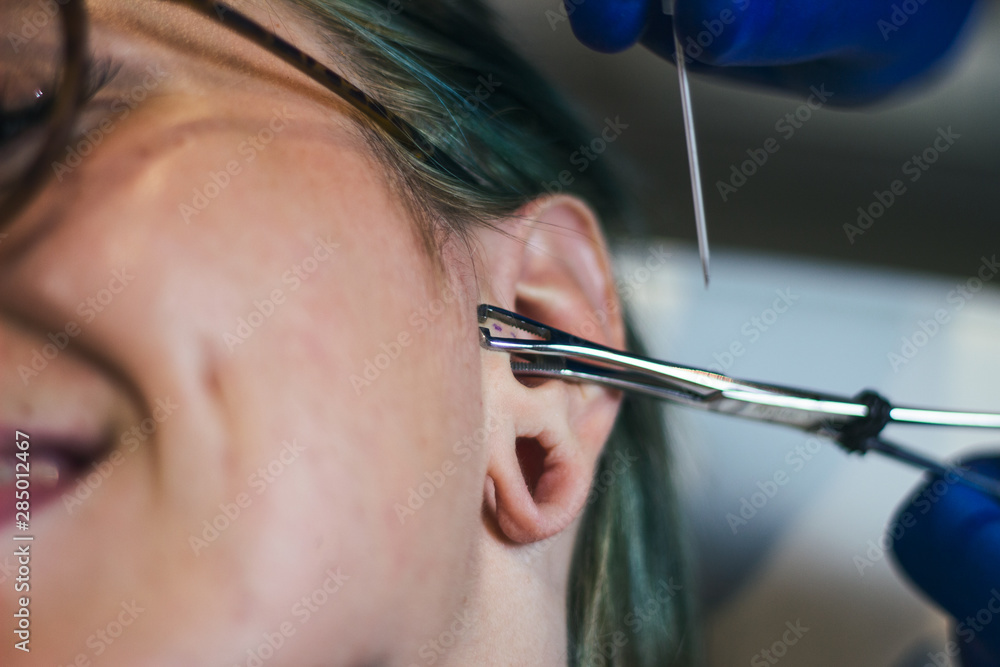 Portrait of a woman getting her ear pierced. Man showing a process of piercing ear . Cleaning
