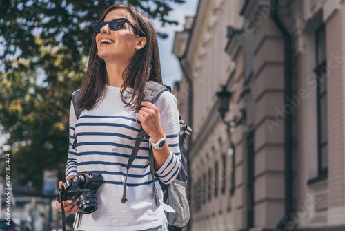 Happy woman in sunglasses with backpack holding digital camera © LIGHTFIELD STUDIOS