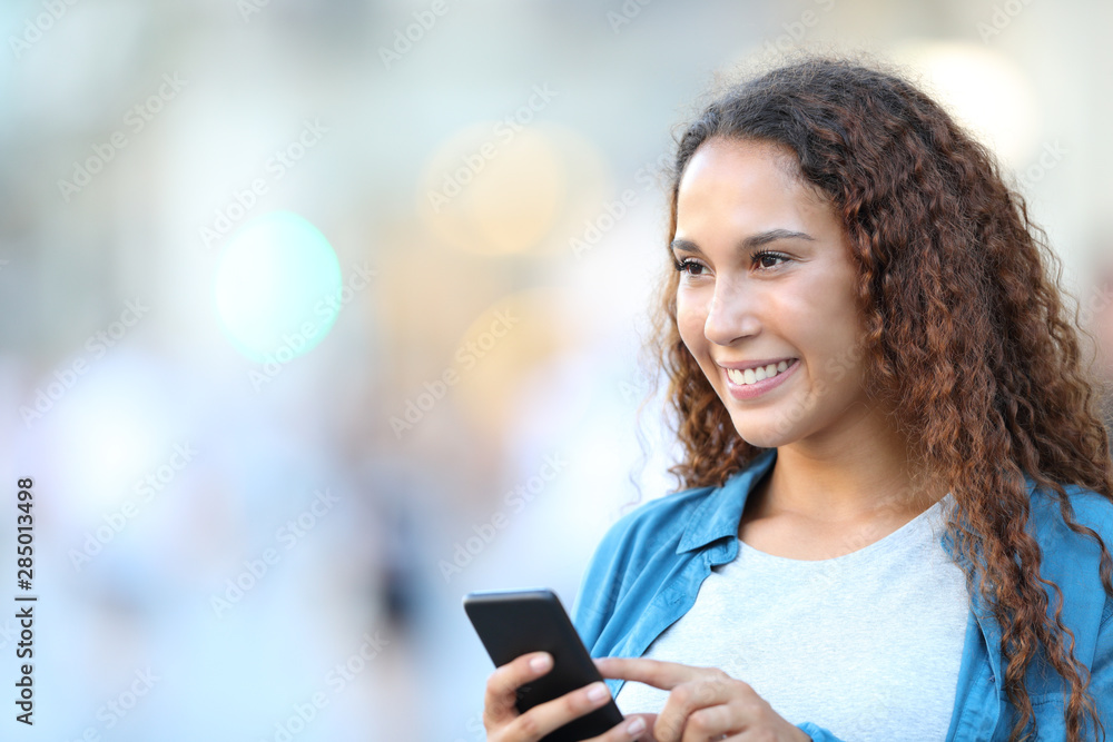 Happy mixed race woman looking away holding phone Happy mixed race woman looking away holding phone
