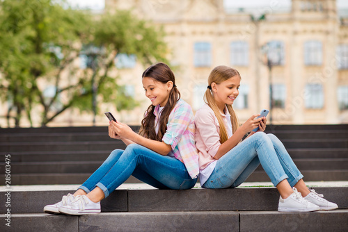 Profile side view of two nice attractive lovely cheerful cheery focused pre-teen girls chatting online internet browsing app 5g spending day weekend rest relax free time outdoors