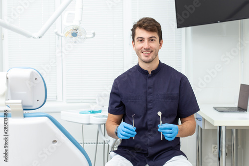 Handsome man wearing blue gloves holds dental probe and mirror in hands
