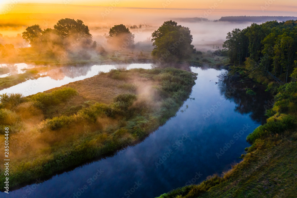 Amazing rural landscape. Blue river flows in countryside. Thick fog in golden sun rays