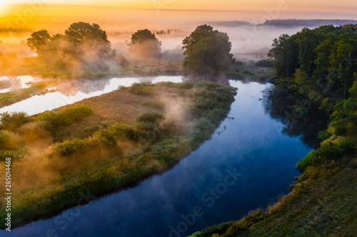 Amazing rural landscape. Blue river flows in countryside. Thick fog in golden sun rays