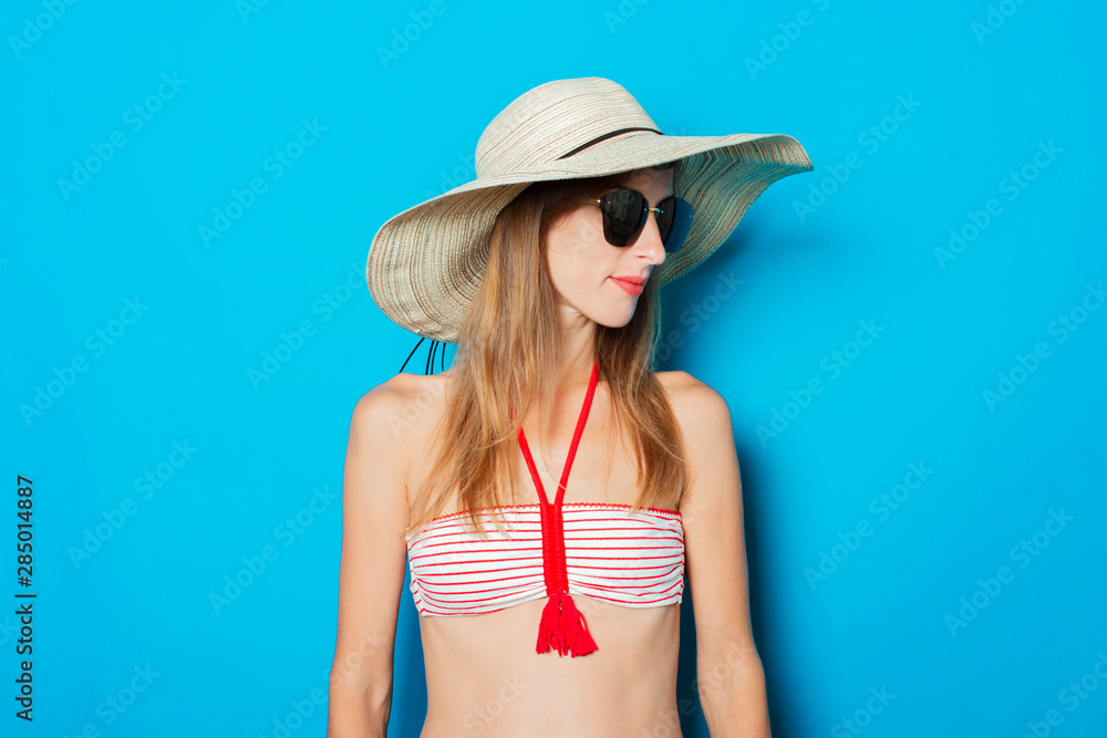 Young woman in a swimsuit, glasses and a wide-brimmed hat on a blue background. Concept of vacation, summer, vacation at sea Young woman in a swimsuit, glasses and a wide-brimmed hat on a blue background. Concept of vacation, summer, vacation at sea