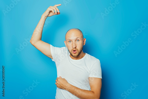 Young man in a white T-shirt with wet armpits from sweat on a blue background. Concept of excessive sweating, heat, deodorant photo