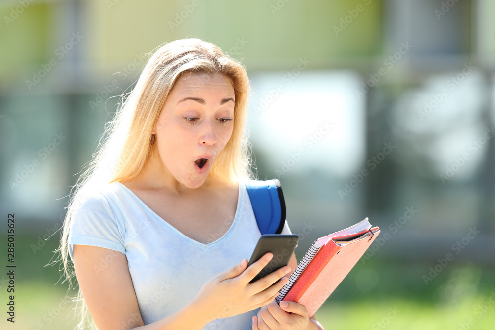 Amazed student checking phone content in a campus Amazed student checking phone content in a campus