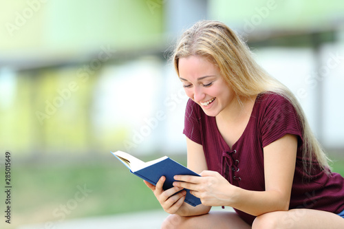 Happy student studying reading a book outdoors