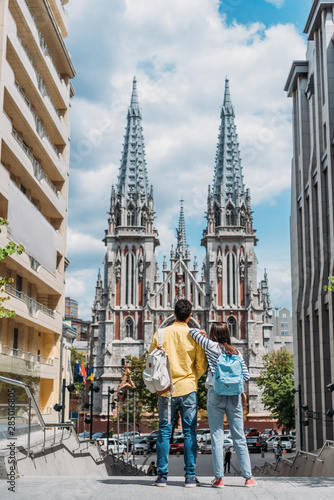 KYIV, UKRAINE - JULY 8, 2019: back view of girl and mixed race man standing near St. Nicholas Roman Catholic Cathedral