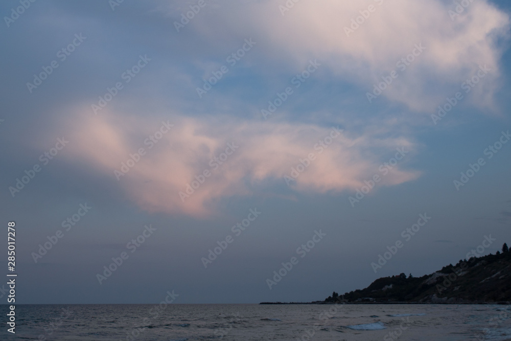 Evening landscape - sunset on the sea, view of the seaside city, blue and pink clouds in the sky