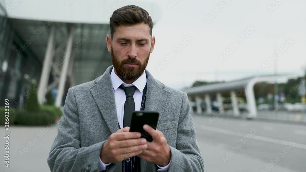 Businessman using smartphone and smiling at airport. Young business executive with mobile phone at airport. Businessman using smartphone and smiling at airport. Young business executive with mobile phone at airport.