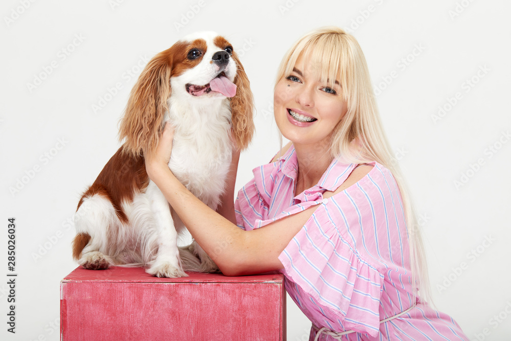 Φωτογραφία Portrait of smiling young blond woman embracing king Charles spaniel dog