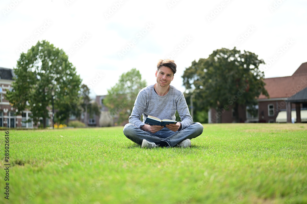 Happy and smiling young man reading a book in a small green park in the Netherlands Happy and smiling young man reading a book in a small green park in the Netherlands