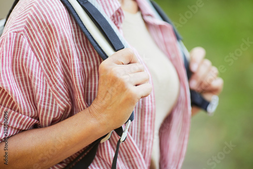 Close-up of mature woman in checked shirt standing with backpack behind her back outdoors